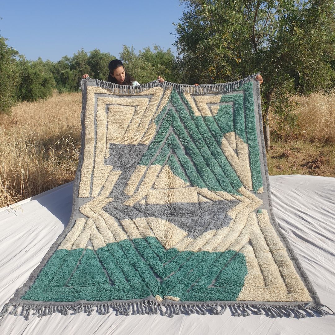 Person holding up a luxurious Beni Mrirt Moroccan rug outdoors, showing its 203×294 cm size with a striking architectural composition — bold teal emerald green concentric diamond and rectangle frames on a cream ivory wool background with soft grey lavender triangular accents, the thick plush Beni Mrirt pile clearly visible