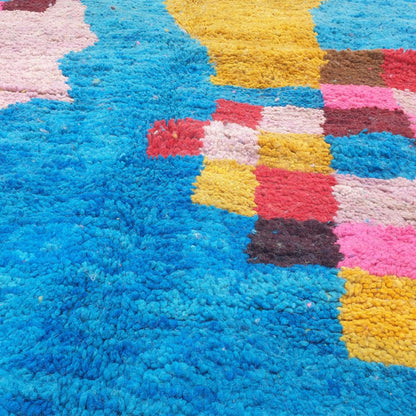 Close-up of a handwoven Boujad Berber rug showing thick natural wool pile in electric teal blue with bold abstract painted-looking shapes in hot pink, red, mustard yellow, lime green and lavender grey — a contemporary Moroccan rug with extraordinary colour depth