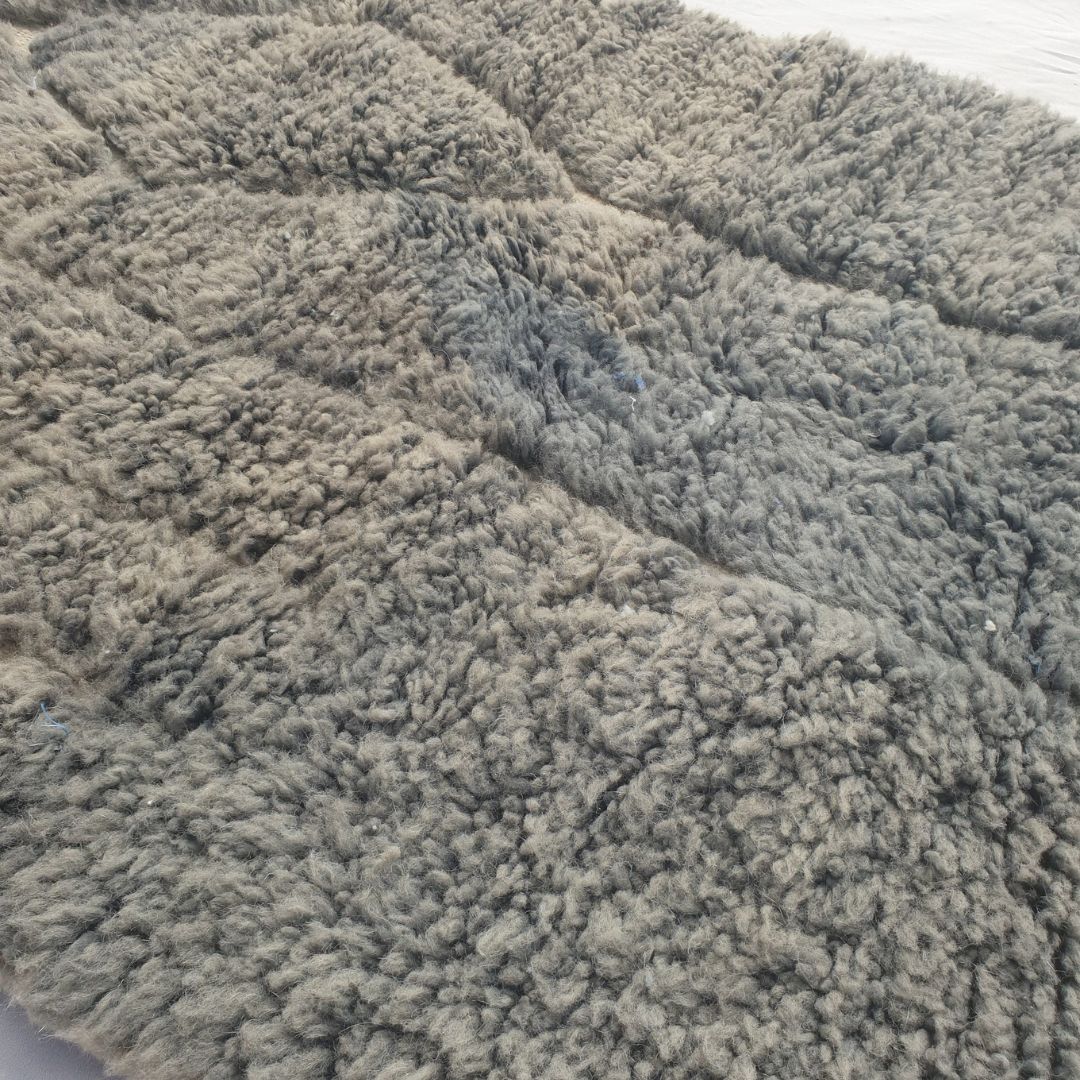Close-up of a Minayta grey taupe Beni Ourain accent rug showing the soft natural wool pile with the dark architectural line composition - the stepped vertical frame and the diamond accent visible against the muted green field, a small-scale abstract composition handwoven in 100% natural wool