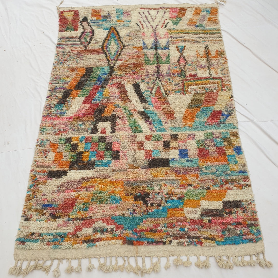 Authentic Moroccan rug 187x307 cm laid flat outdoors - ivory ground densely scattered with multicolor confetti flecks, a checkerboard band and diamond motifs, transitioning into a busier saturated patchwork lower section, handwoven in Morocco