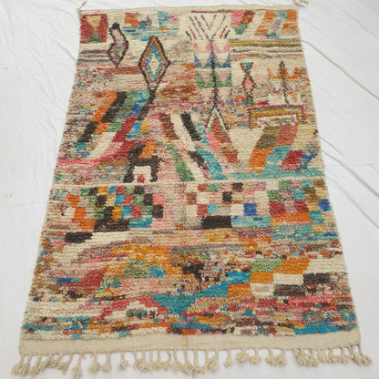 Authentic Moroccan rug 187x307 cm laid flat outdoors - ivory ground densely scattered with multicolor confetti flecks, a checkerboard band and diamond motifs, transitioning into a busier saturated patchwork lower section, handwoven in Morocco