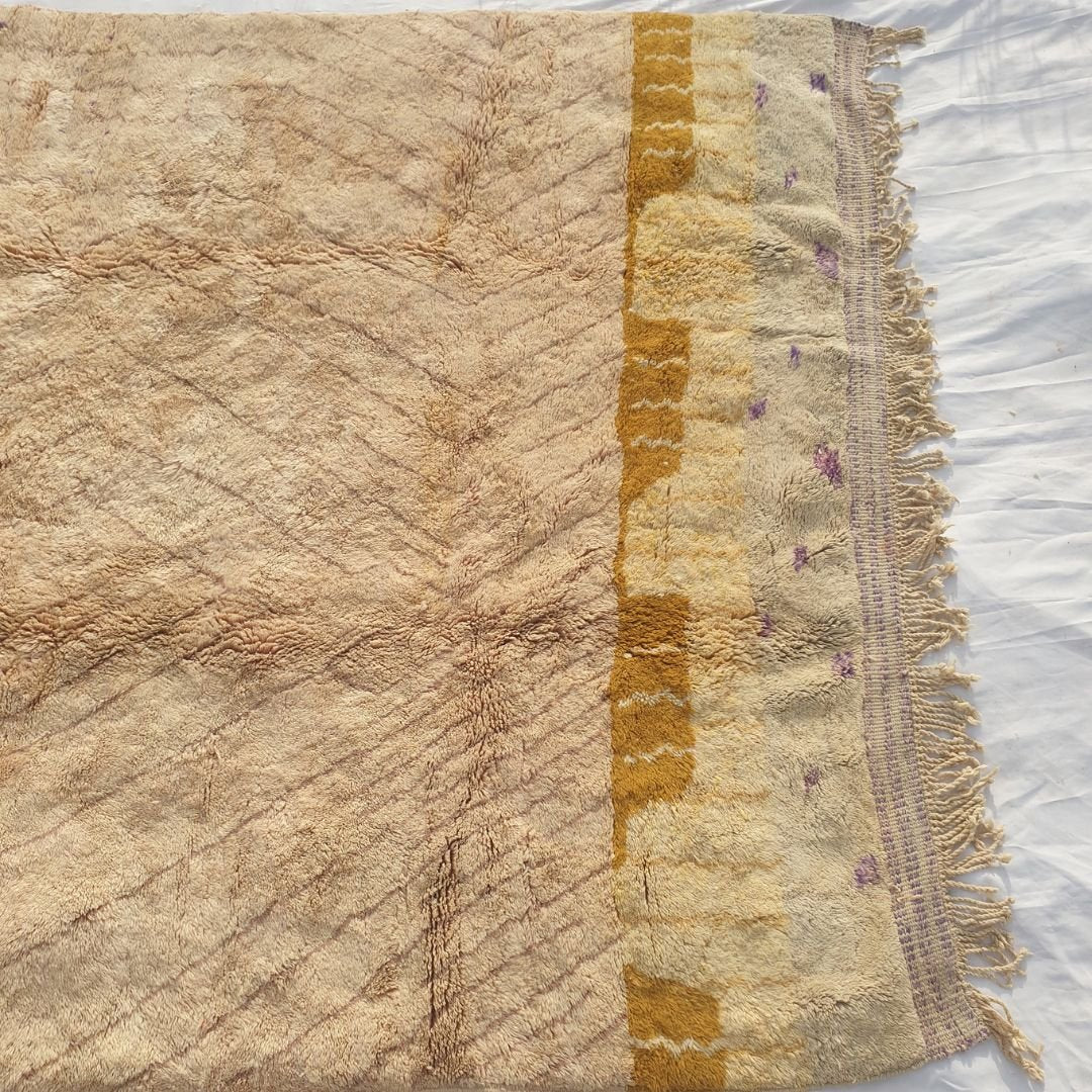 Warm yellow and purple details contrasting with the soft pale nude pink field highlighting the dense weave of the Moroccan wool rug