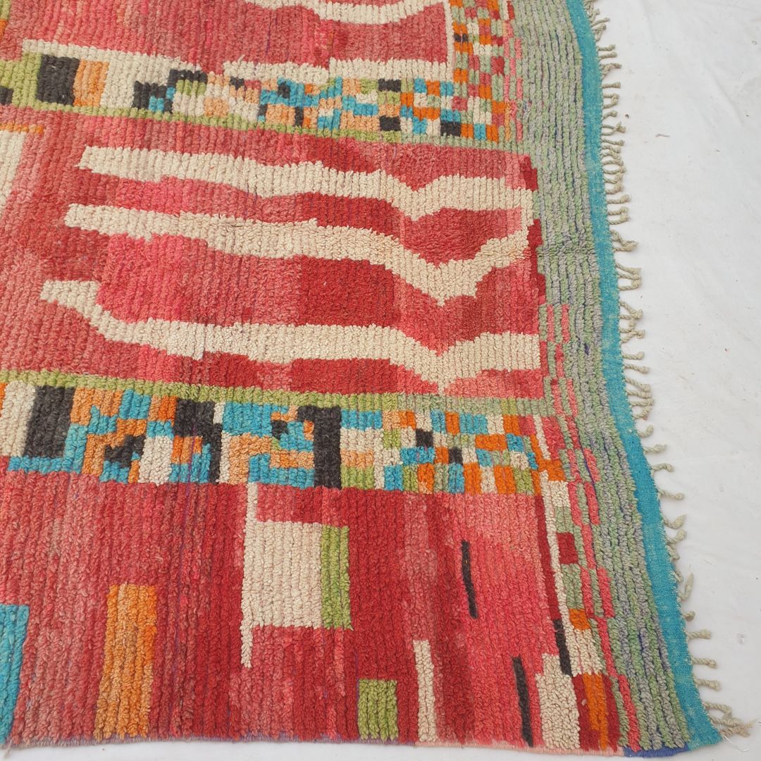 Bottom half of a luxurious Moroccan wool rug featuring dense handknotted red pile with vibrant multicolor motifs and natural fringe, showcasing the soft thick texture of authentic Berber craftsmanship