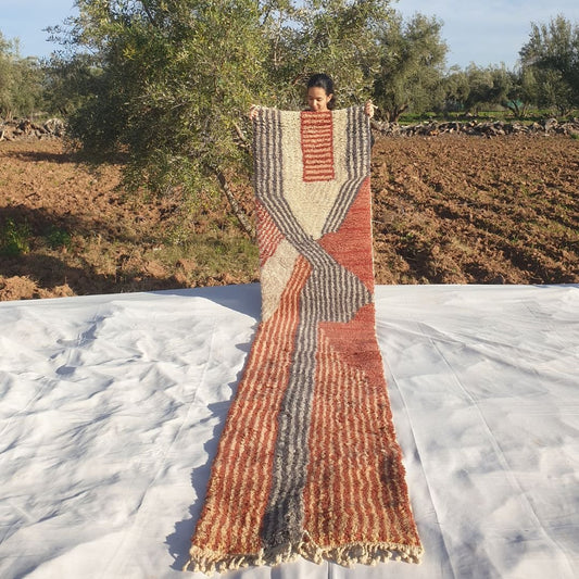 Luxury 2x12 Beni Mrirt Moroccan runner rug with abstract terracotta orange, beige, and gray striped wavy patterns held outdoors in olive grove