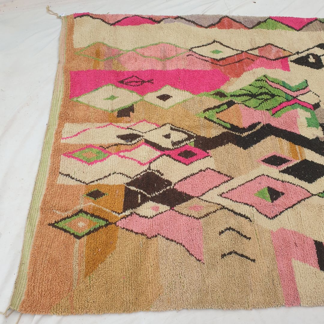 Top half of a luxurious cream Moroccan wool rug featuring dense handknotted pile with large black abstract shapes, pink and white diamond motifs, and a vivid multicolor striped band in green, blue and pink with natural fringe — showcasing the soft thick texture of authentic Berber craftsmanship
