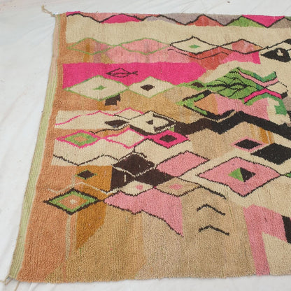 Top half of a luxurious cream Moroccan wool rug featuring dense handknotted pile with large black abstract shapes, pink and white diamond motifs, and a vivid multicolor striped band in green, blue and pink with natural fringe — showcasing the soft thick texture of authentic Berber craftsmanship
