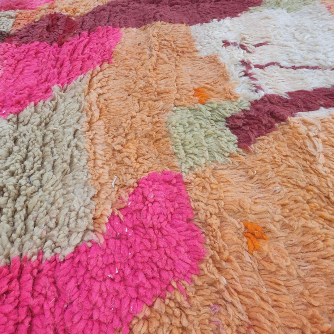 Close-up of Claha Boujad Moroccan rug showing the dramatic burgundy abstract figure with a diamond waist on a warm peach-apricot wool ground, with sage green horizontal bands above.