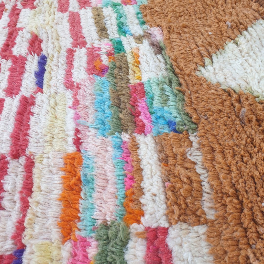 Close-up of Clahma Boujad Moroccan rug showing intricate teal floral motifs on a red field, striped bands, and three ivory diamond shapes on a warm brown background.
