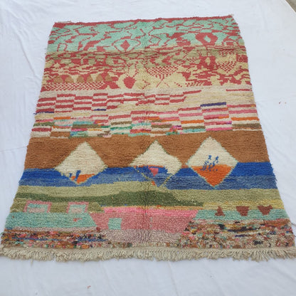 Handwoven Boujad Berber rug (216x278 cm) laid flat, displaying a vivid abstract landscape in red, teal, brown, blue, olive and pastel tones, with natural fringe.