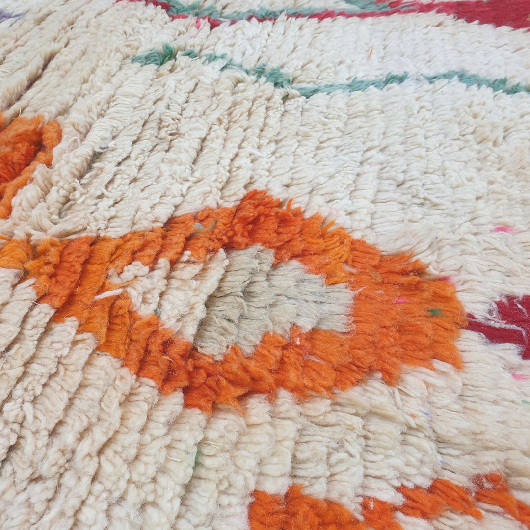 Close-up of Dialca Boujad Moroccan rug showing the striking large central elongated diamond with concentric rings in orange, purple, grey and green on an ivory wool field.

