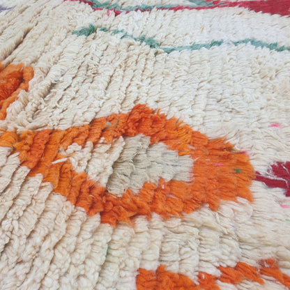 Close-up of Dialca Boujad Moroccan rug showing the striking large central elongated diamond with concentric rings in orange, purple, grey and green on an ivory wool field.
