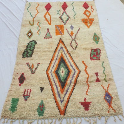 Dialca – handwoven Boujad Berber rug (190x310 cm) laid flat on white, ivory field scattered with colourful tribal motifs — large central diamond, orange diamonds, green shapes and red symbols.
