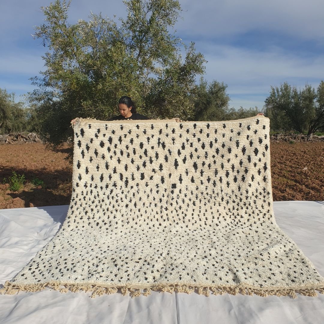 Handwoven 8x10 Boujad Moroccan rug featuring black abstract geometric motifs on cream white background held outdoors