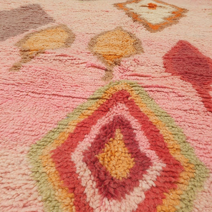 Close-up of a Hadita Moroccan rug showing the soft wool pile with the pendant and leaf motifs against the rose pink field - the scattered shapes in olive, red and orange visible against the clear pink ground, handwoven in 100% wool