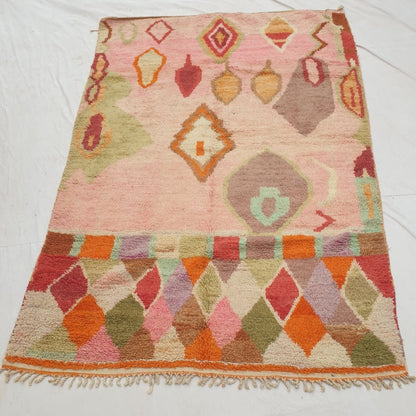 Authentic Moroccan rug 200x303 cm laid flat outdoors - clear rose pink field with scattered pendant motifs above a bright rainbow harlequin diamond border, handwoven in Morocco