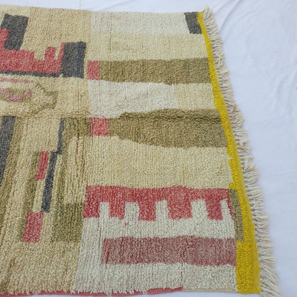 Lower half of Khazo Moroccan Berber rug with tall olive and charcoal column forms rising from a vivid yellow-gold border strip, thick cream fringe and soft ivory wool pile.
