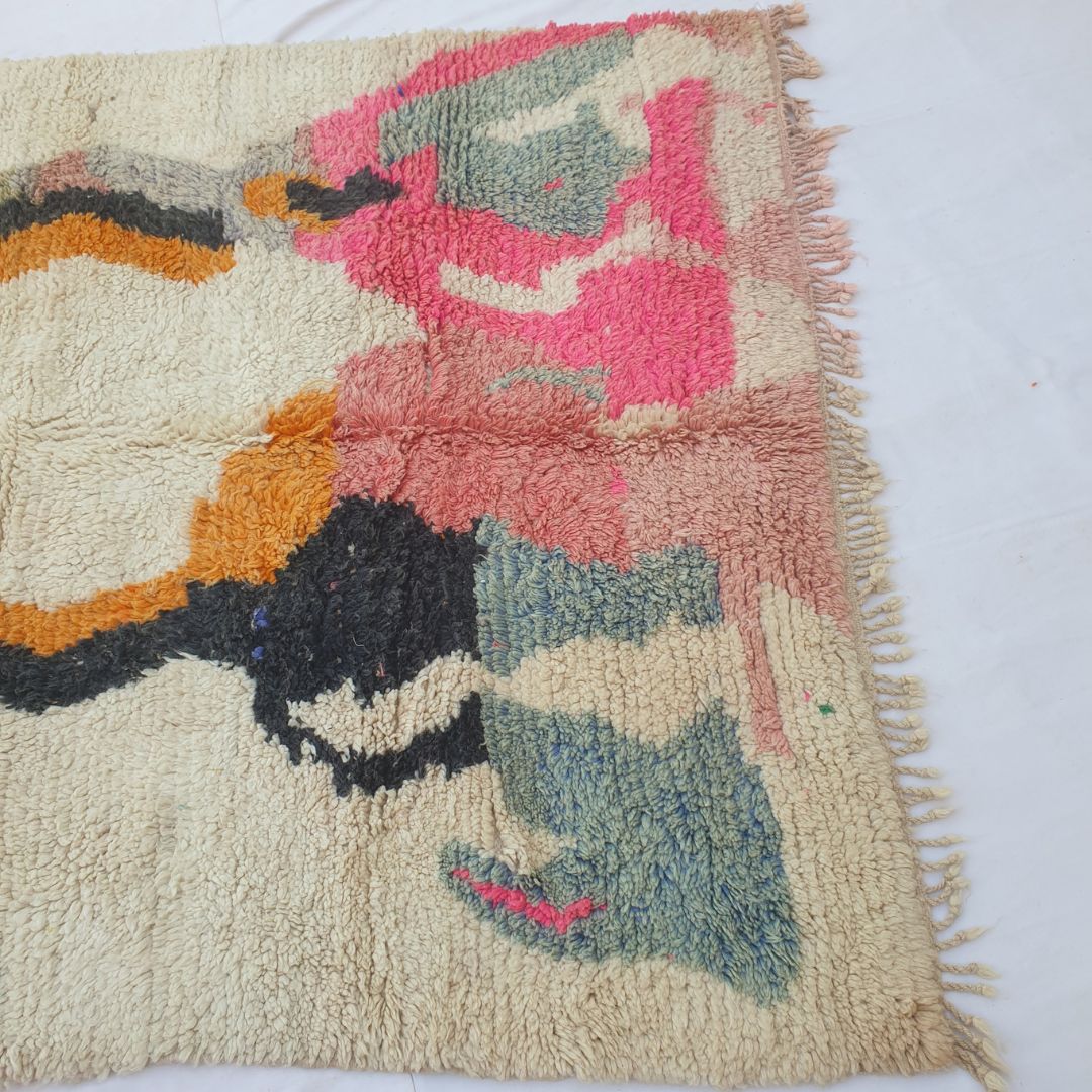 Lower half of Lahca Moroccan Berber rug with large freeform abstract shapes — bold hot pink mass centre-right, slate-blue grey forms on both lower sides, an irregular black blob lower-left, and golden-yellow centre accent — on an open ivory field in dense hand-knotted wool with pink-toned fringe.
