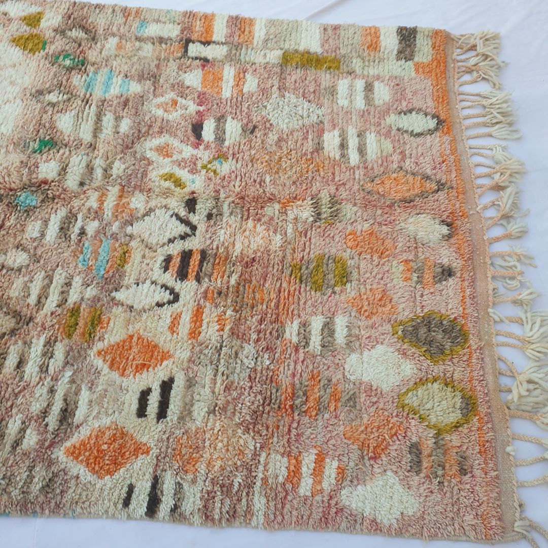 Lower half of Lahnac Moroccan Azilal rug with warm terracotta-pink ground, scattered ivory cream ovals, mustard gold diamonds, orange accents and dark brown details in thick, soft hand-knotted wool pile with cream fringe.