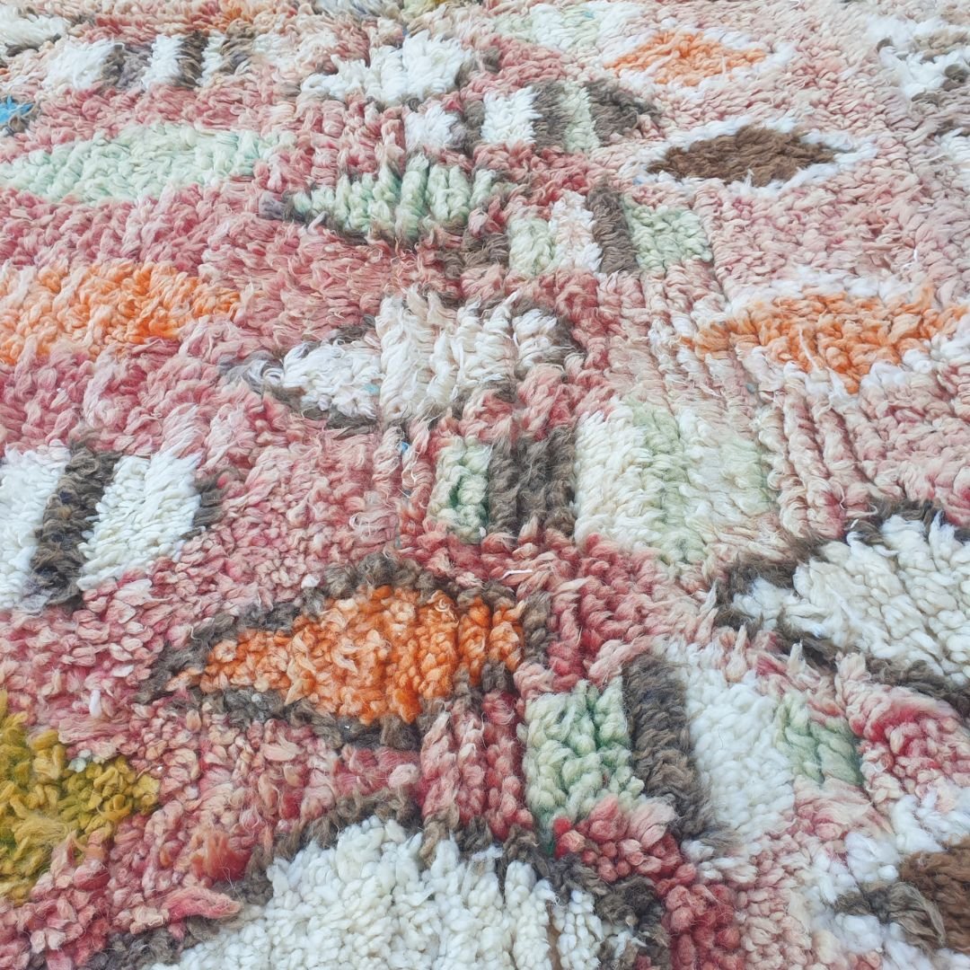 Close-up of Lahnac Moroccan Berber rug showing intricate scattered diamond, oval and geometric motifs in ivory cream, mustard, teal/turquoise, orange and dark brown on a rose-blush wool field.