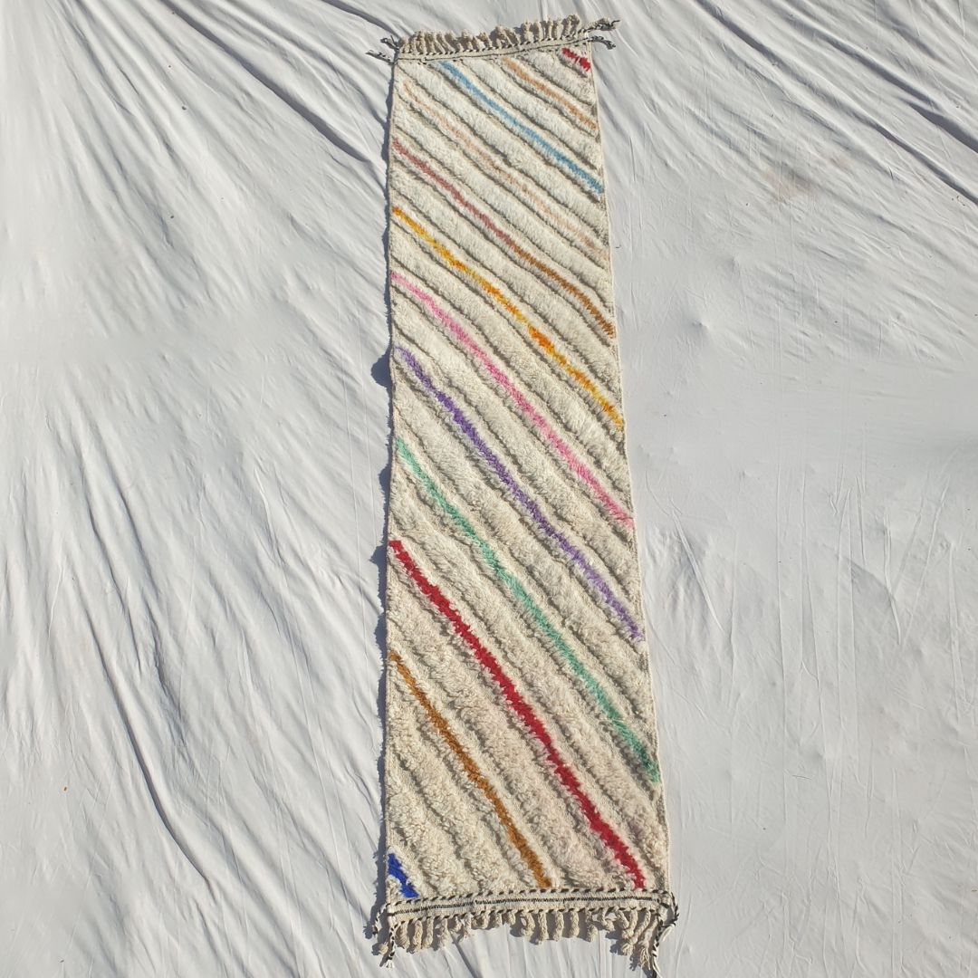 Authentic Beni Ourain Moroccan runner rug 73x303 cm laid flat - white cream natural wool base with bold multicolor diagonal stripes in yellow, orange, pink, purple, teal, red and blue running at an angle across the full field, handwoven in Morocco by Beni Ourain Berber women