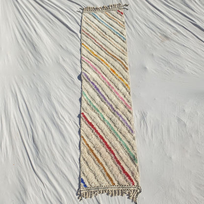 Authentic Beni Ourain Moroccan runner rug 73x303 cm laid flat - white cream natural wool base with bold multicolor diagonal stripes in yellow, orange, pink, purple, teal, red and blue running at an angle across the full field, handwoven in Morocco by Beni Ourain Berber women