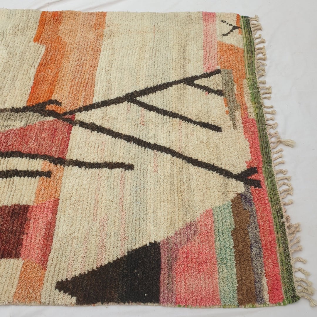 Detail shot of the colour field transitions on Macla Moroccan rug - the orange, red and brown horizontal bands at the top of the rug meeting the cream ground below, with the artist's confident brush-like colour blocking visible in the wool
