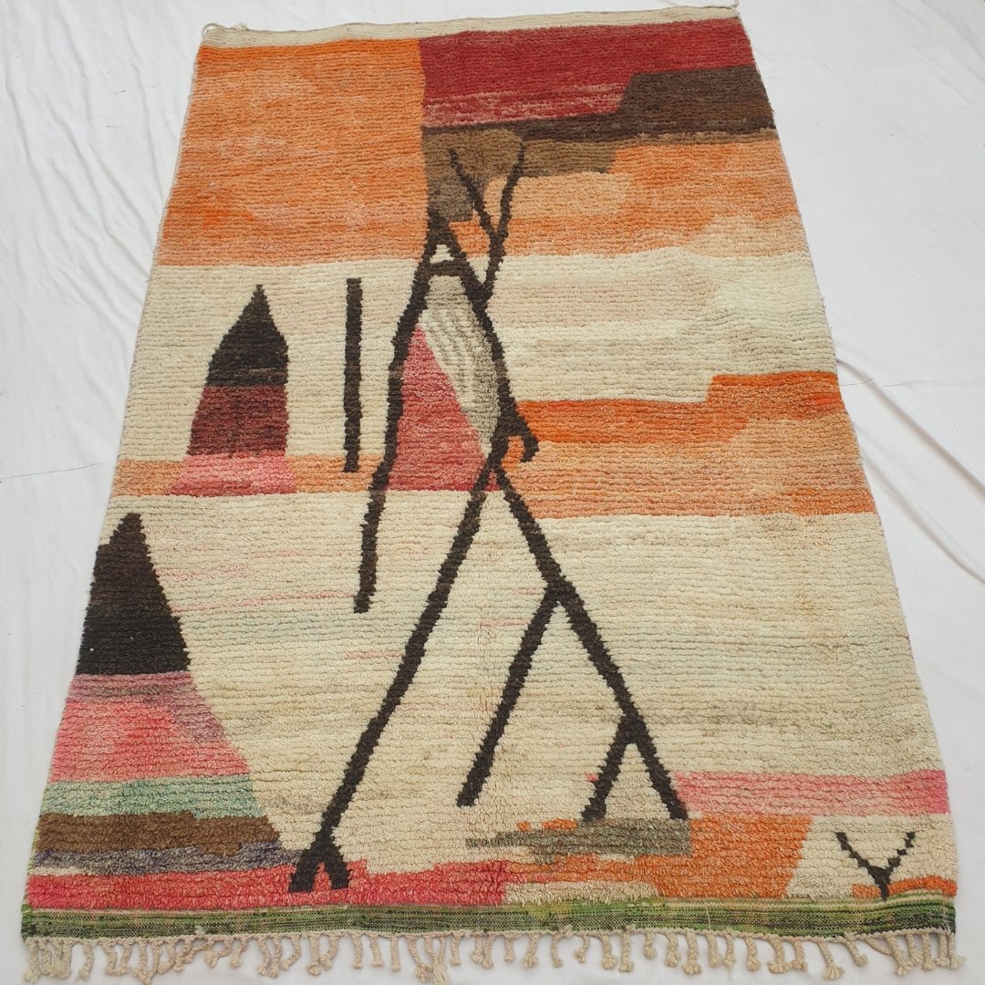 Authentic Moroccan rug 197x315 cm laid flat outdoors - orange and red colour fields, a bold abstract dark line composition, and a vivid multicolour striped border with green kilim flat-weave edge, handwoven in Morocco
