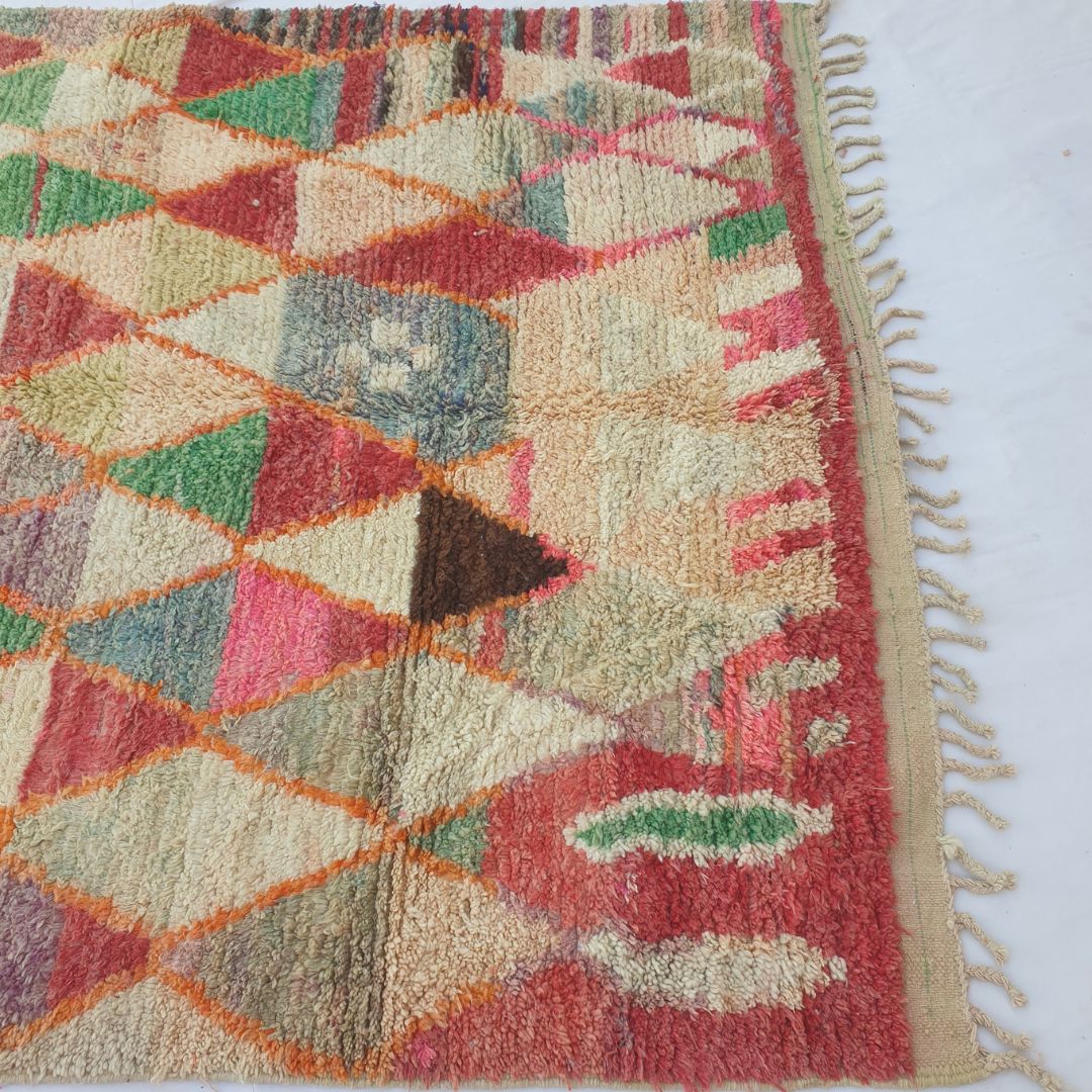Lower half of Motaca Moroccan Berber rug where the geometric triangle lattice dissolves into looser abstract forms — scattered green oval, red blocks and cream fields — in thick shaggy hand-knotted wool pile with natural fringe.
