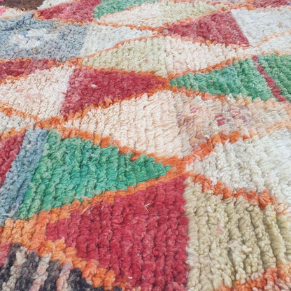Close-up of Motaca Boujad Moroccan rug showing the intricate harlequin triangle grid pattern — each orange-outlined diamond cell filled with two opposing triangles in contrasting colours including red, sage green, ivory, pink and grey-blue.