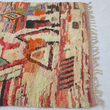 Lower half of Oueca Moroccan Berber rug with rich terracotta-red horizontal stripes, cream fields and scattered purple, orange and brown geometric accents in dense, fluffy wool pile.