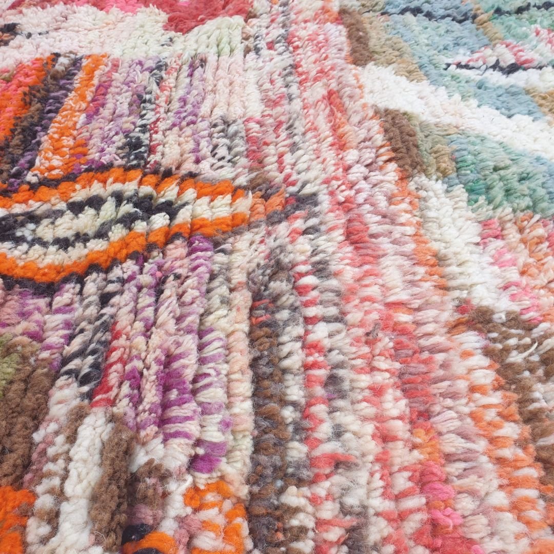 Close-up of Oueca Boujad Moroccan rug showing an orange-outlined triangle with dark brown interior, surrounded by geometric diamonds in orange, green and black.