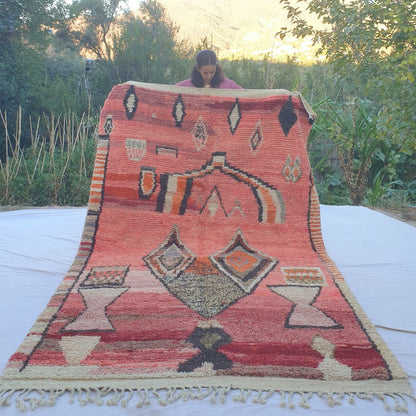 Large 6x10 vibrant coral red Boujad Moroccan rug with bold black, orange and cream Berber symbols held outdoors at sunset