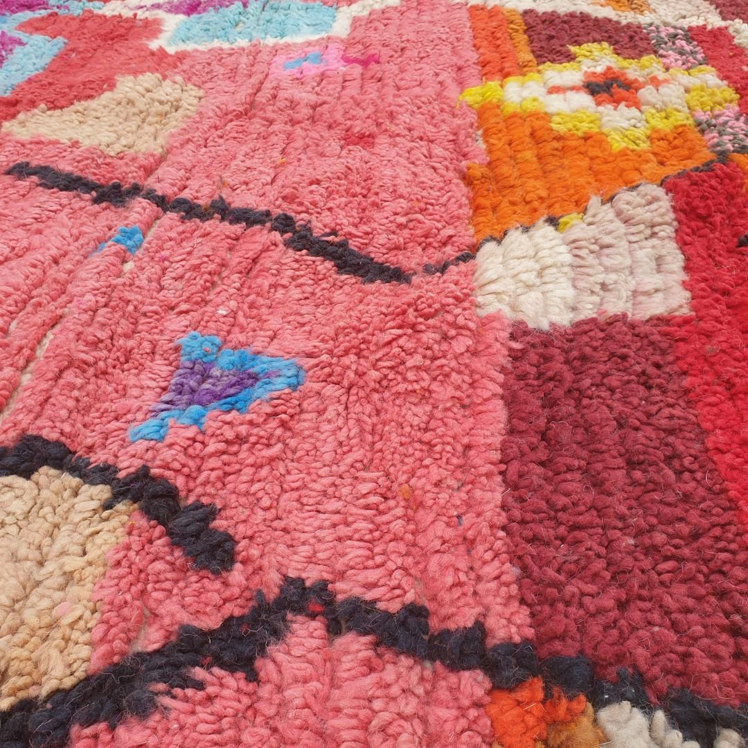 Close-up of a handwoven Boujad Berber rug showing an incredibly rich dense composition of multicolor geometric motifs on a coral pink wool pile — diamonds, stripes, zigzags and small squares in teal, orange, yellow, magenta, blue and green, showcasing exceptional craftsmanship