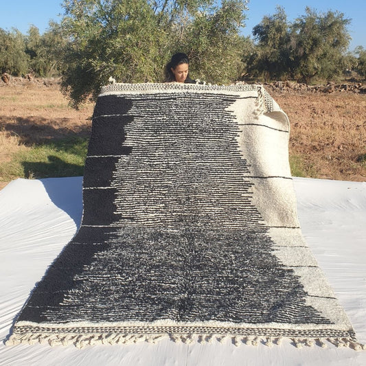 Classic black and white 6x10 Beni Ourain Moroccan rug featuring bold abstract geometric lines and stripes on creamy ivory background, ultra-plush high-pile texture, held outdoors in olive grove at sunset