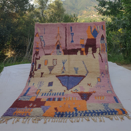 large pink and ivory Boujad Moroccan rug held up in nature, revealing a striking blue triangle centrepiece surrounded by rare figurative symbols in cobalt and orange.