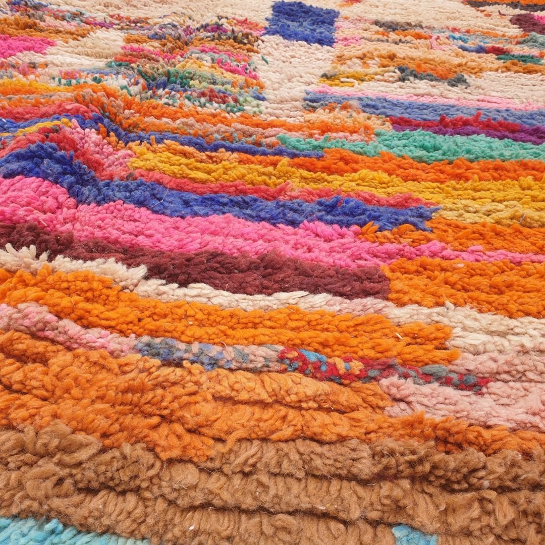 Close-up of a handwoven Boujad Berber rug showing dense horizontal stripe bands in orange, teal, red, pink, blue, yellow and green on a cream wool base — a patchwork mosaic composition of remarkable detail and craftsmanship, with natural wool pile visible in the cream vertical sections