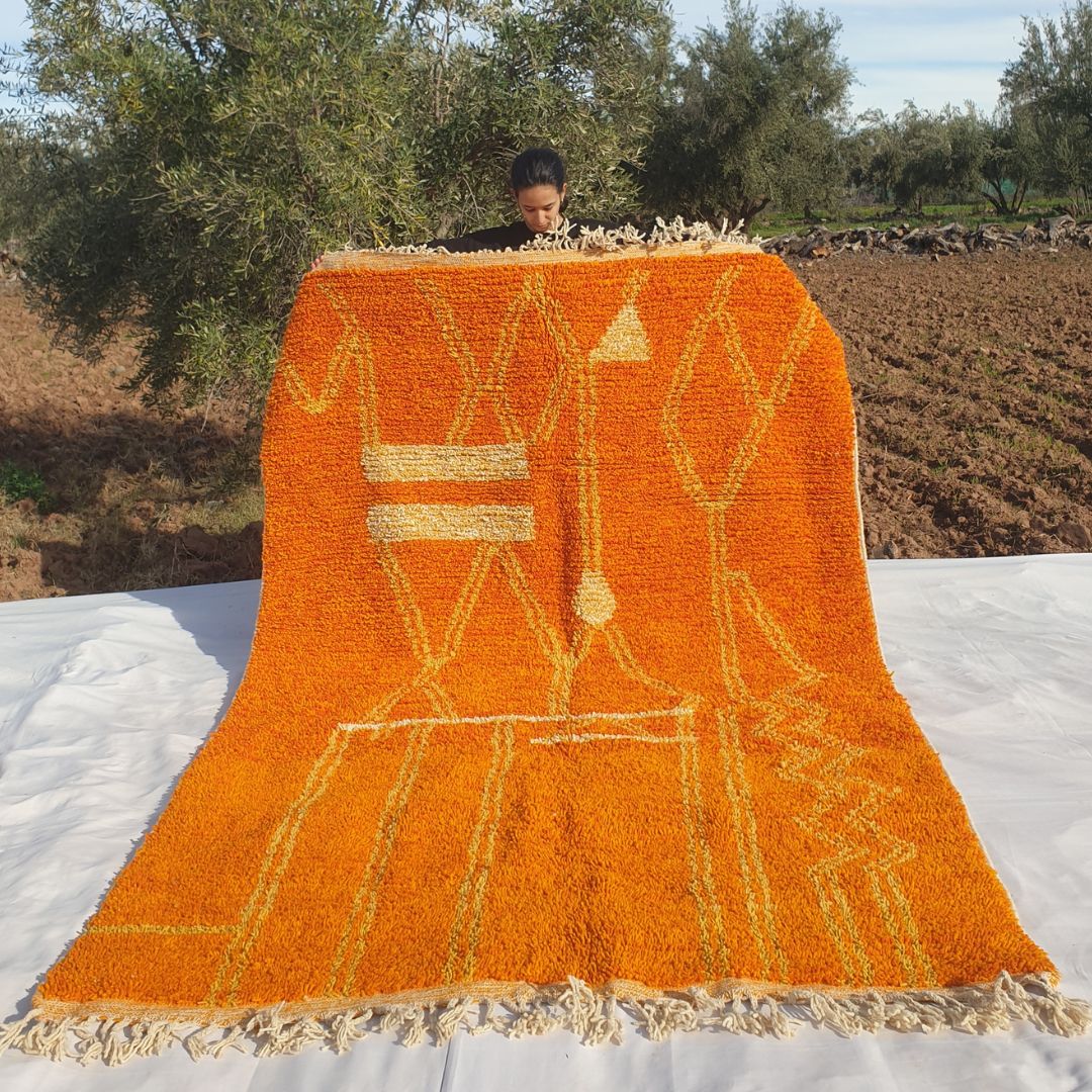 Vibrant 6x10 Boujad Moroccan rug in bright orange with yellow abstract geometric designs held outdoors in olive grove