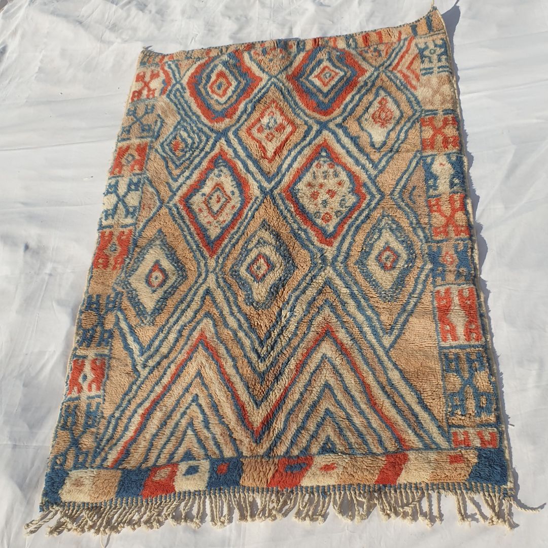 Intricate red and blue diamond accents with beige background highlighting fluffy weave of high-end Moroccan plush rug