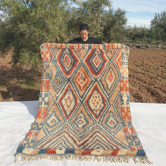 Luxury 5x7 Beni Mrirt Moroccan rug featuring vibrant geometric diamond patterns in blue, red, and beige on plush shag wool base held outdoors