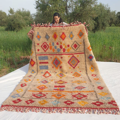 Handwoven 6x9 Beni Mrirt Moroccan rug with vibrant multicolored diamond geometric patterns in red, blue, orange, yellow on beige held outdoors