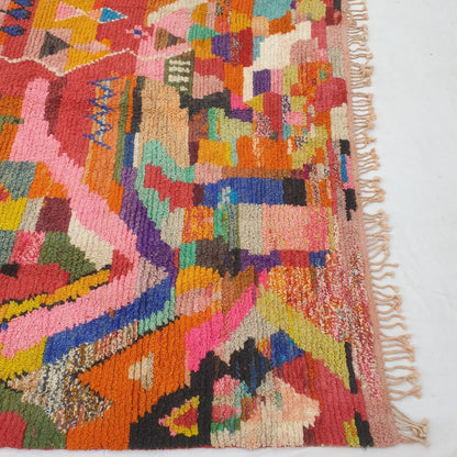 Bottom half of a large maximalist Moroccan wool rug featuring a thick handknotted pile bursting with hundreds of multicolor geometric shapes in every colour of the spectrum — orange, red, pink, blue, green, yellow and purple — with natural fringe, showing extraordinary softness and density
