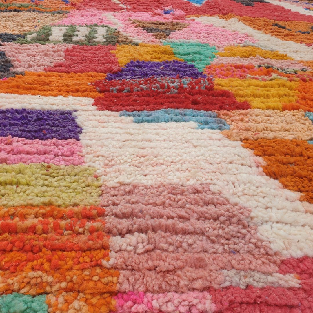 Close-up of a handwoven Boujad Berber rug showing an incredibly dense all-over composition of multicolor geometric motifs — diamonds, triangles, zigzags and abstract shapes in orange, hot pink, cobalt blue, teal, purple and lime green on a 100% natural wool pile